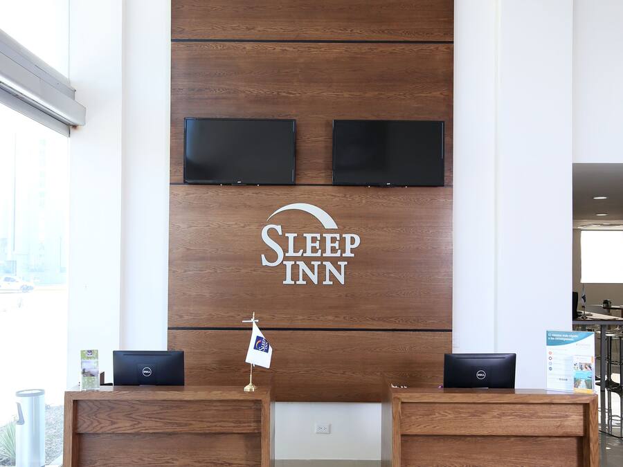 Una reception con un pannello di legno e uno schermo televisivo, una bandiera e un cartello per Sleep Inn.
