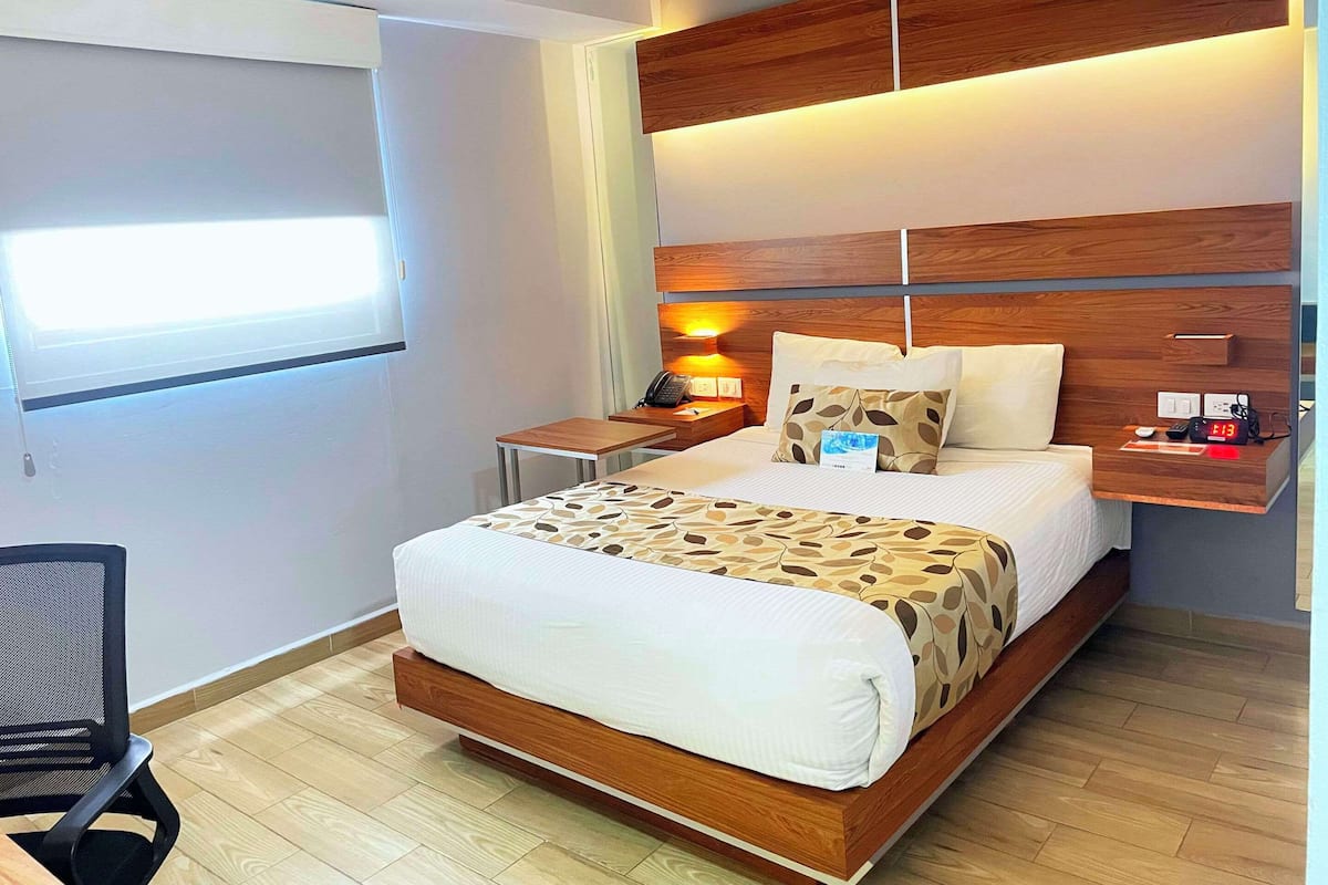 A modern hotel room with a wooden headboard, a bedside table with a lamp, a phone, and a clock.