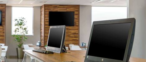 A modern office with two desktop computers on a wooden desk, a potted plant, and a TV on the wall.