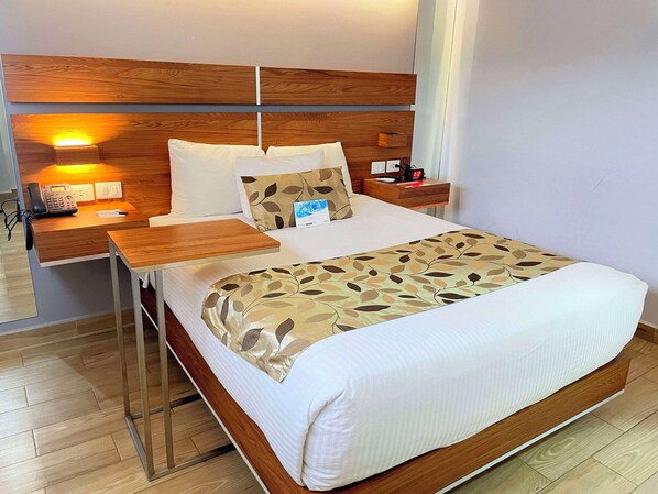 Une chambre d’hôtel avec un grand lit, une tête de lit en bois, une table de chevet avec une lampe, un téléphone et une petite table de nuit avec une horloge.