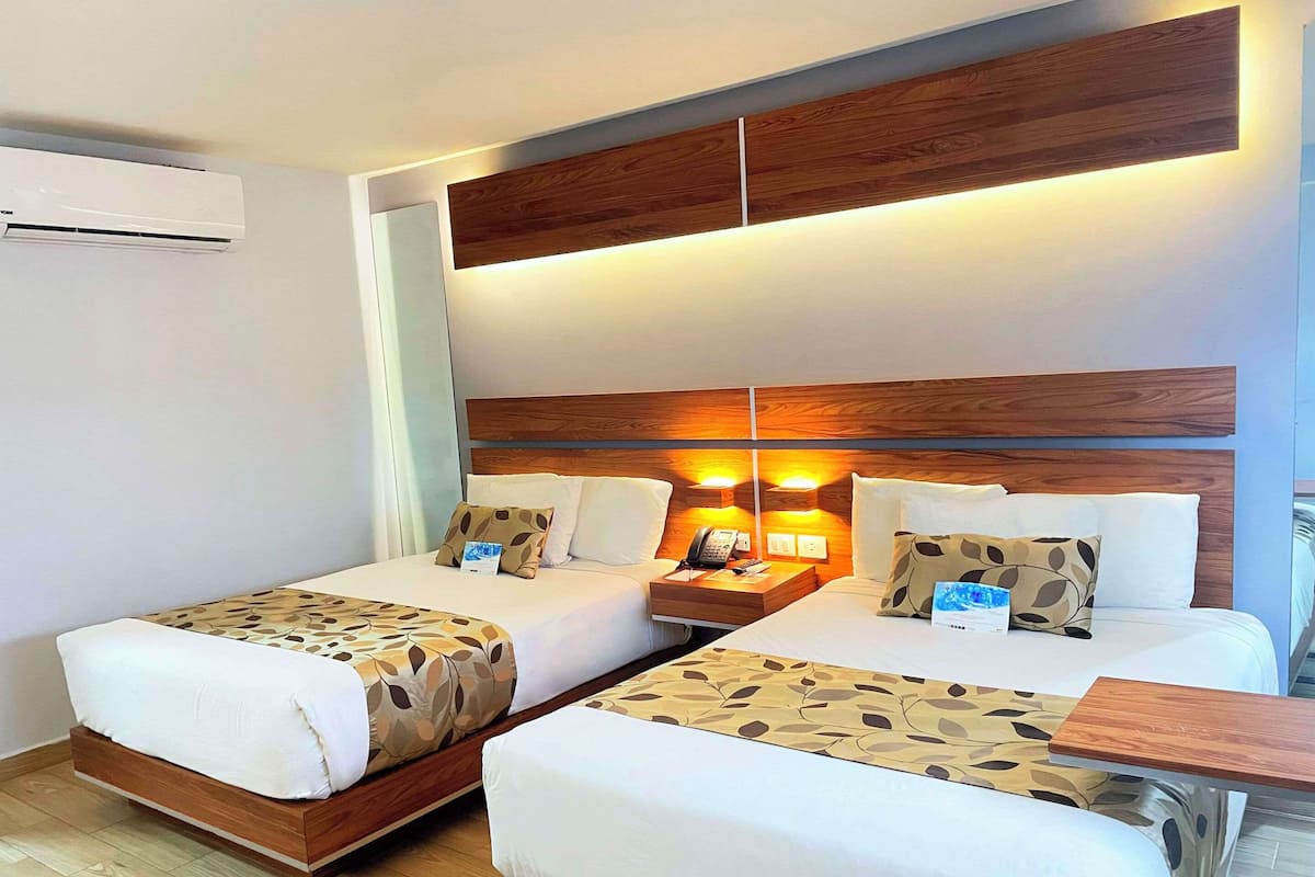 A hotel room with two beds, a wooden headboard, bedside lamps, a nightstand, and a small table.