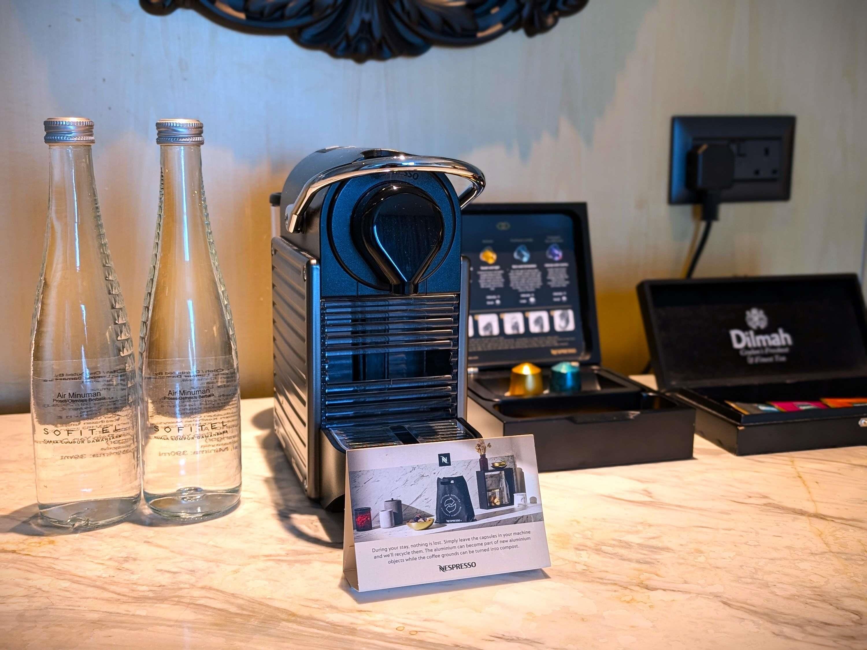 A coffee machine, two water bottles, a Nespresso machine, and a sign about recycling.