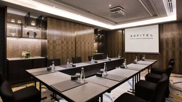 A conference room with a long table, chairs, a projector screen, and a wooden accent wall.