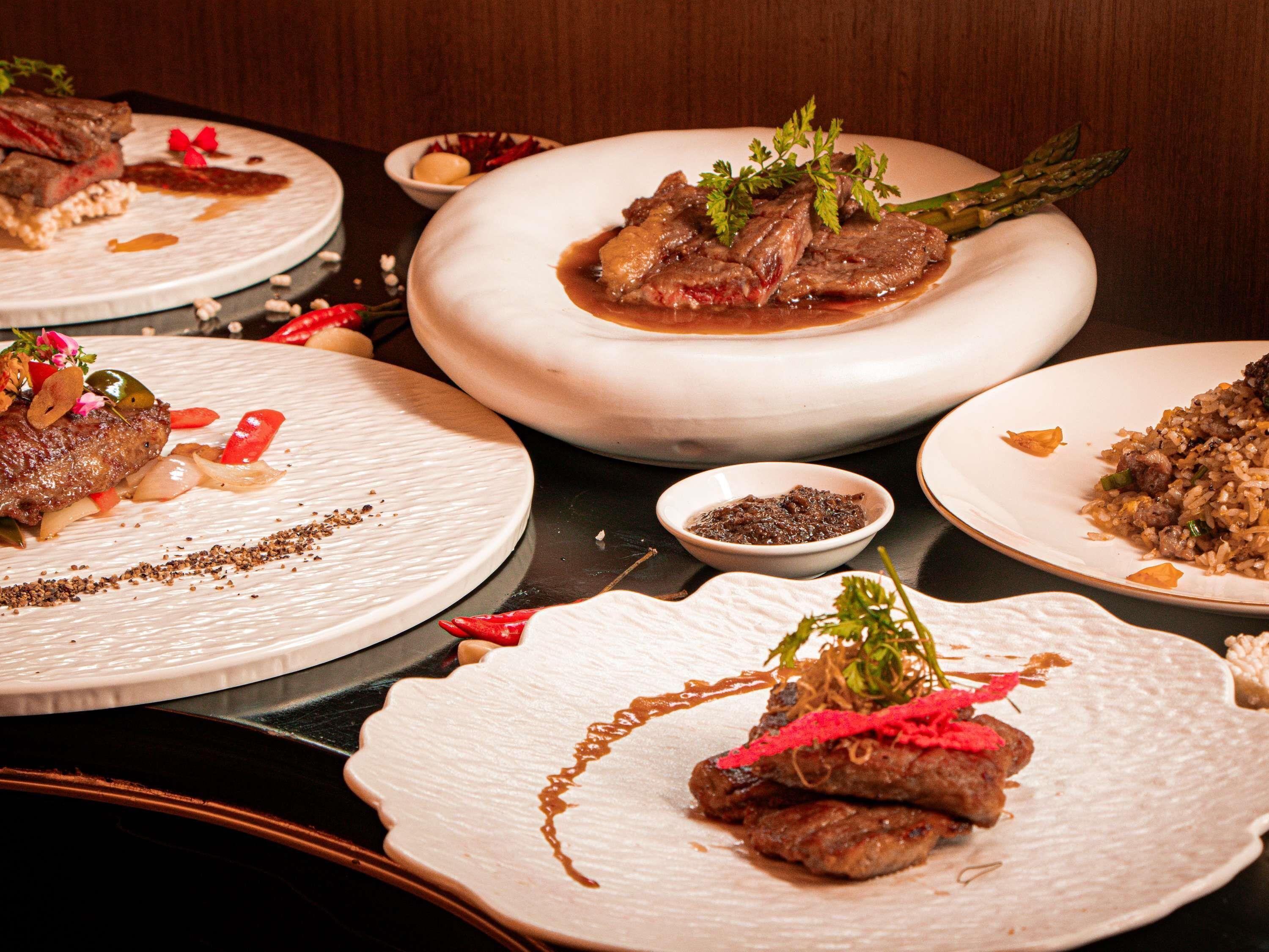 A variety of dishes on plates, including meat and vegetables, with garnishes and sauces.