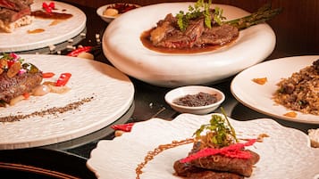 A variety of dishes on plates, including meat and vegetables, with garnishes and sauces.