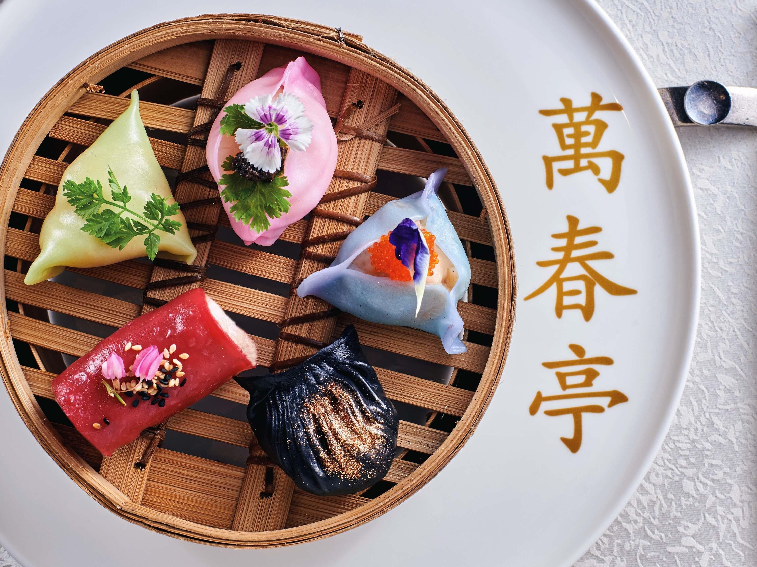 A bamboo steamer basket with various dumplings on a plate.