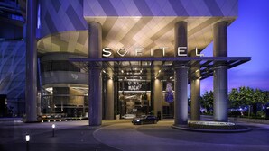 Una entrada de hotel moderna con un llamativo letrero de "SOFITEL", grandes columnas y un camino de acceso circular.