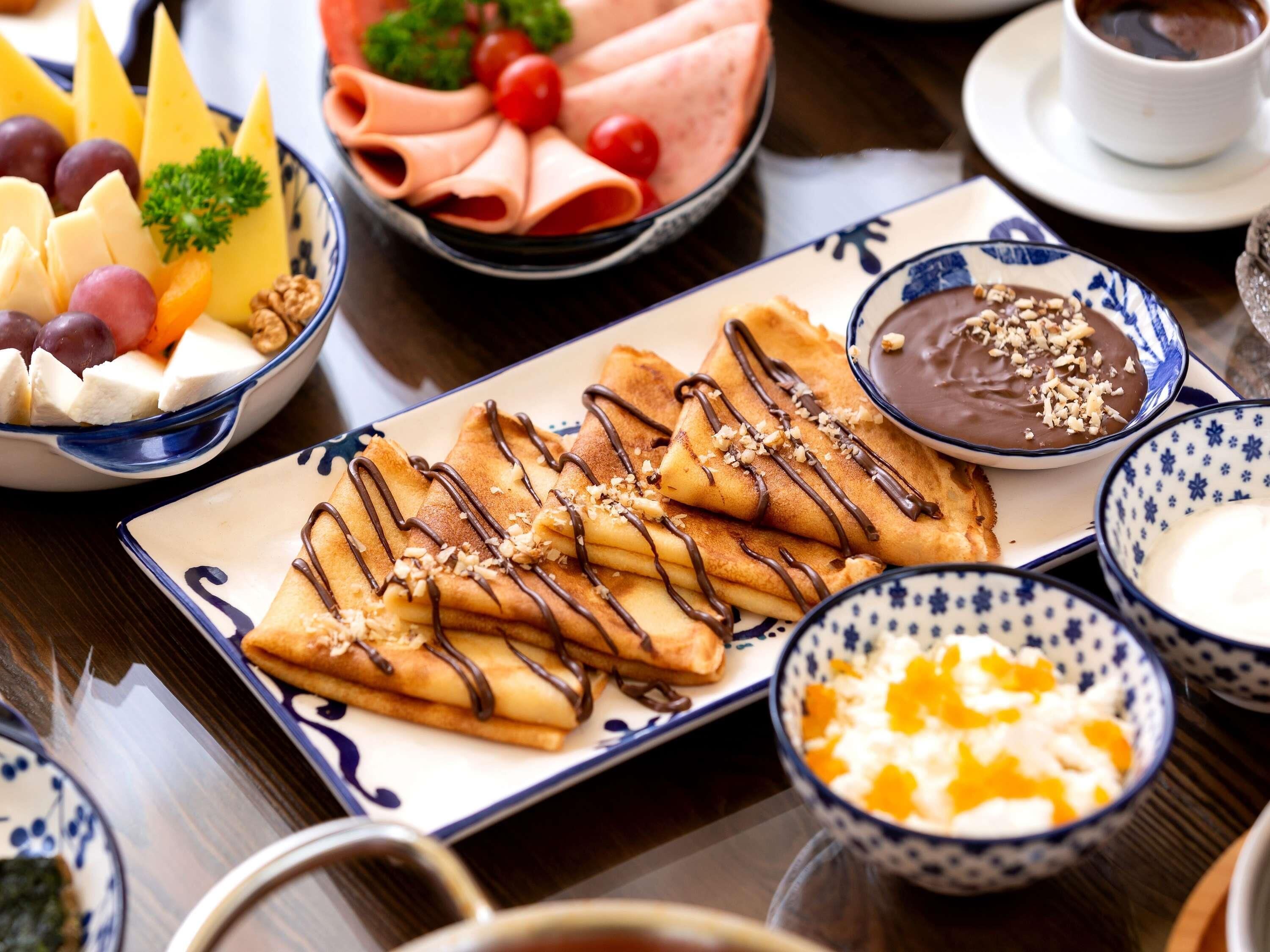 Uma mesa com diversos alimentos, incluindo crepes, queijo, frutas e uma tigela de sopa.