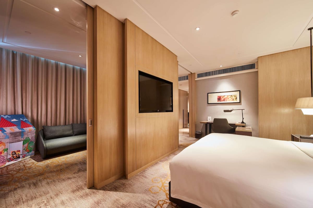 Een hotelkamer met een groot bed, een bank, een aan de muur bevestigde televisie en een bureau met lamp.