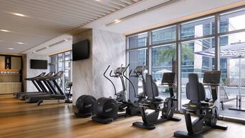 A gym with treadmills, elliptical machines, and a TV on the wall.