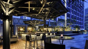 An outdoor bar area with wooden flooring, black metal chairs, and umbrellas providing shade.