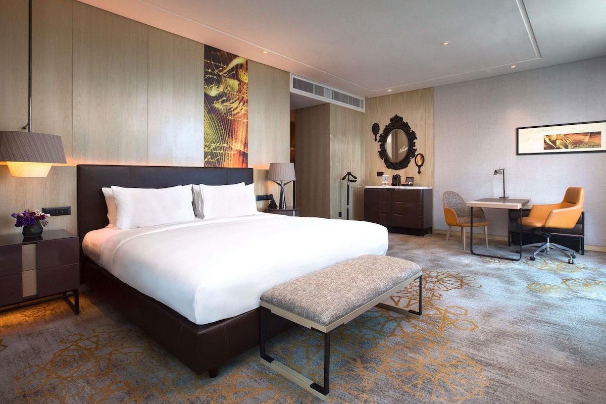 A modern hotel room with a large bed, bedside tables, a desk, and a chair.