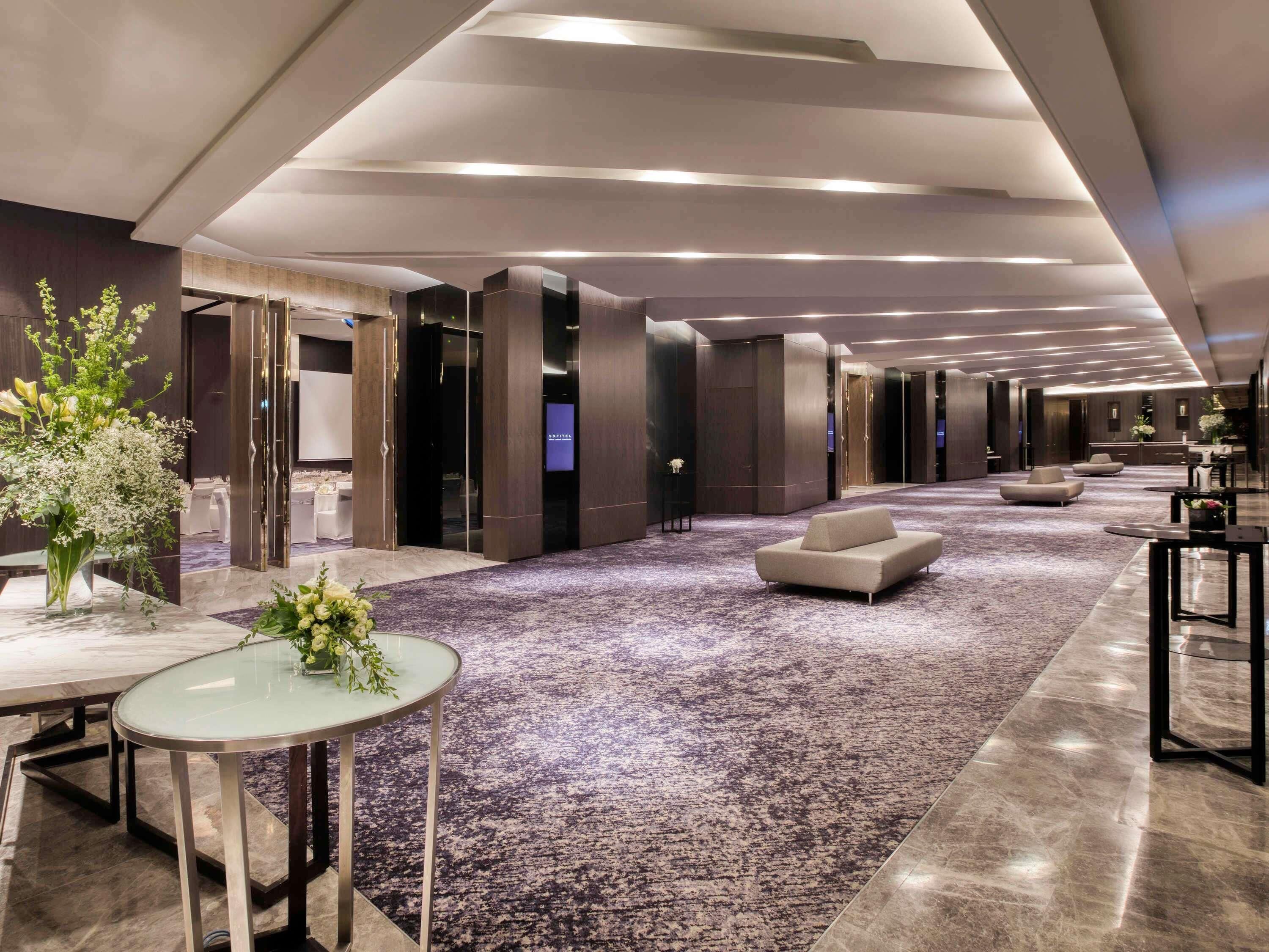 Un vestíbulo amplio con piso alfombrado, zonas de estar y una mesa de vidrio.