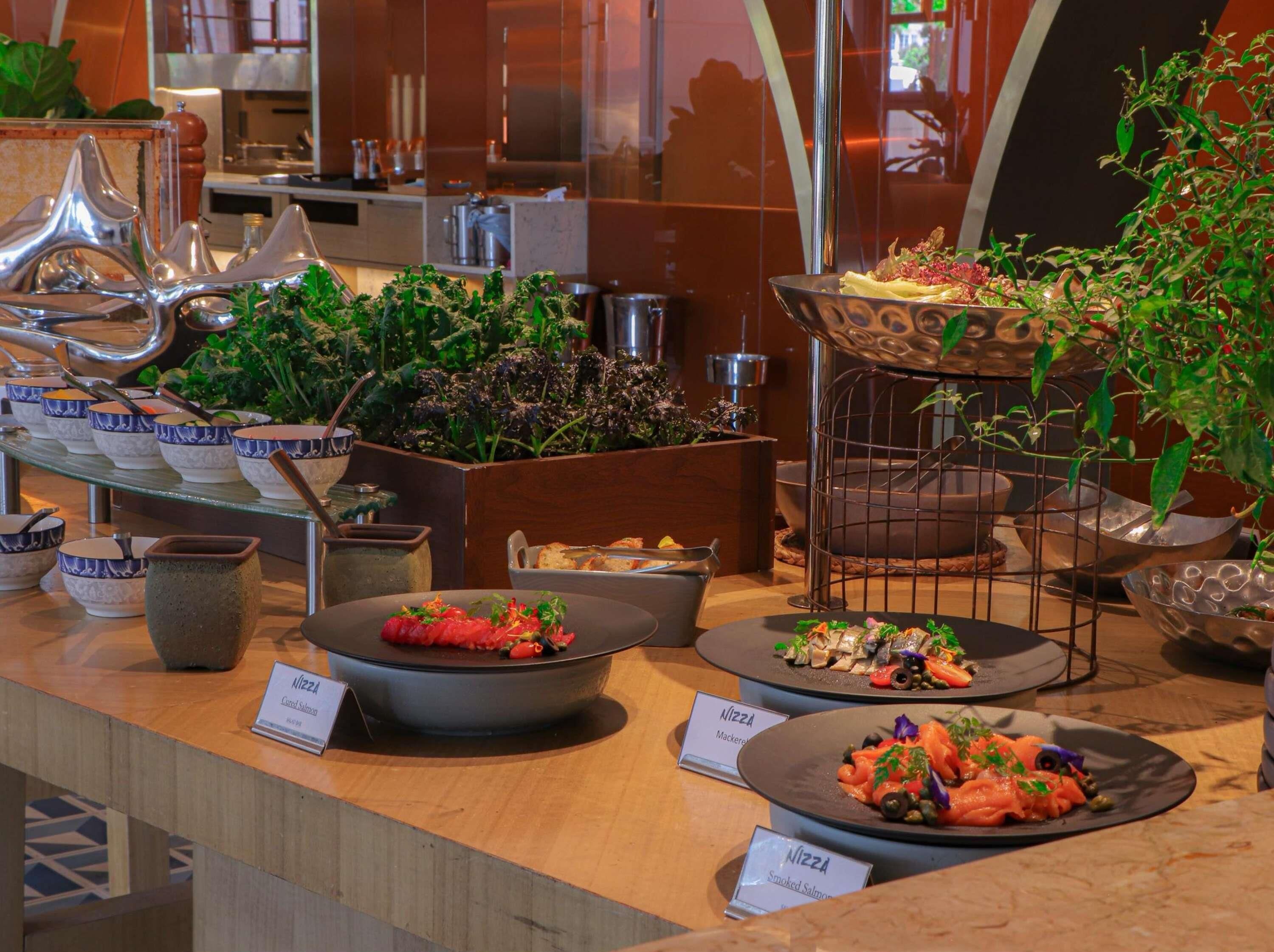 Un espace buffet proposant divers plats, notamment de la salade niçoise, du maquereau et du saumon fumé.