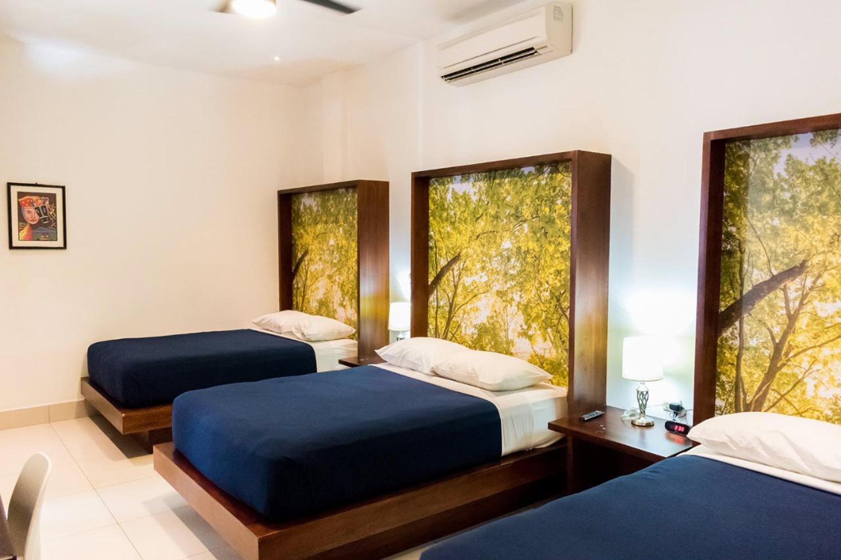A hotel room with three beds, each with a wooden headboard and a tree-themed wall mural.