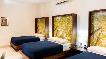 A hotel room with three beds, each with a wooden headboard and a tree-themed wall mural.