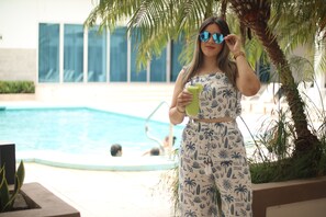 A person standing by a pool with palm trees, holding a drink. - Hotel Agualcas (Managua)