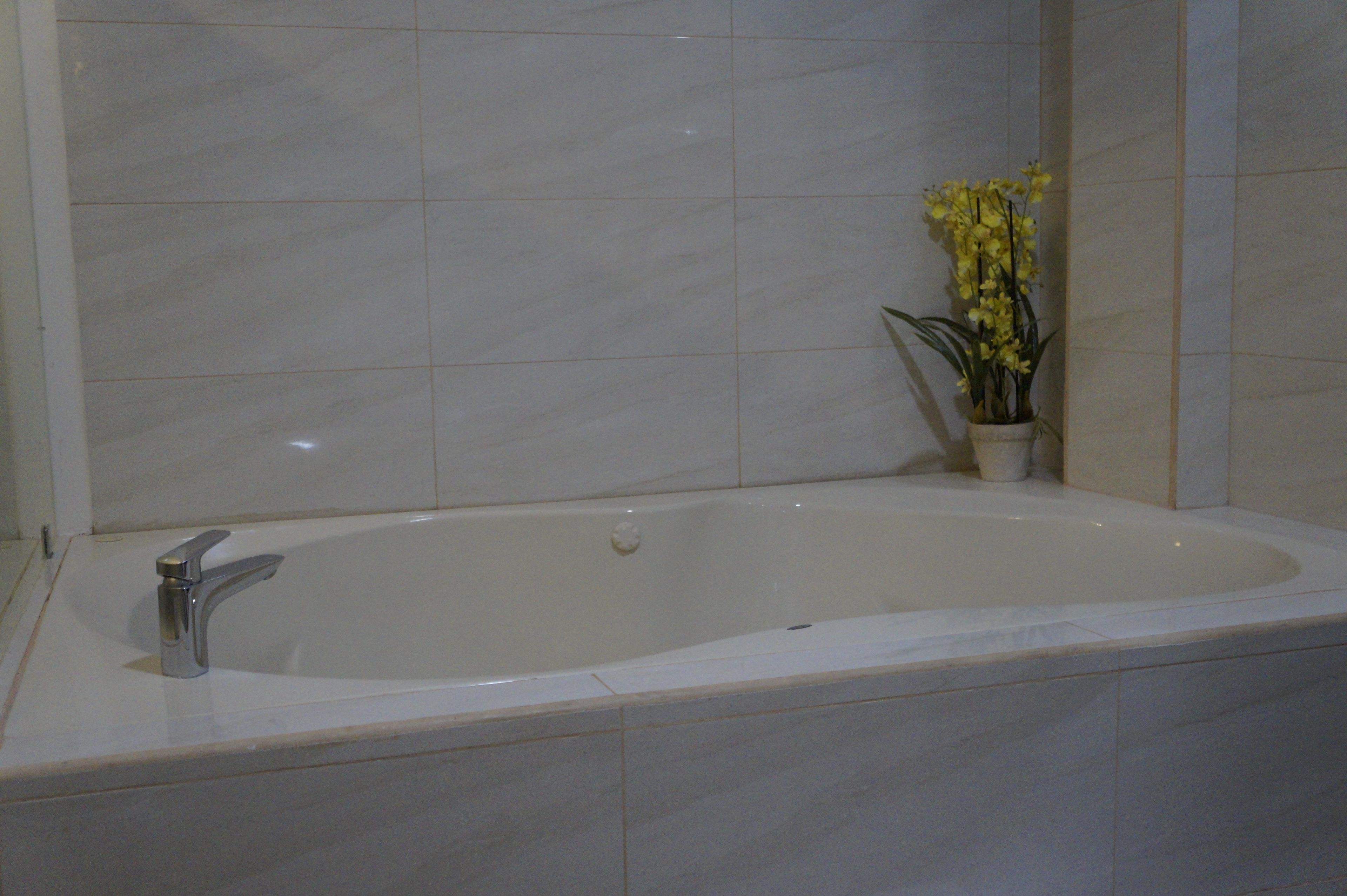 Ein Badezimmer mit einer großen Badewanne, einem modernen Wasserhahn und einem Topf mit gelben Blüten.