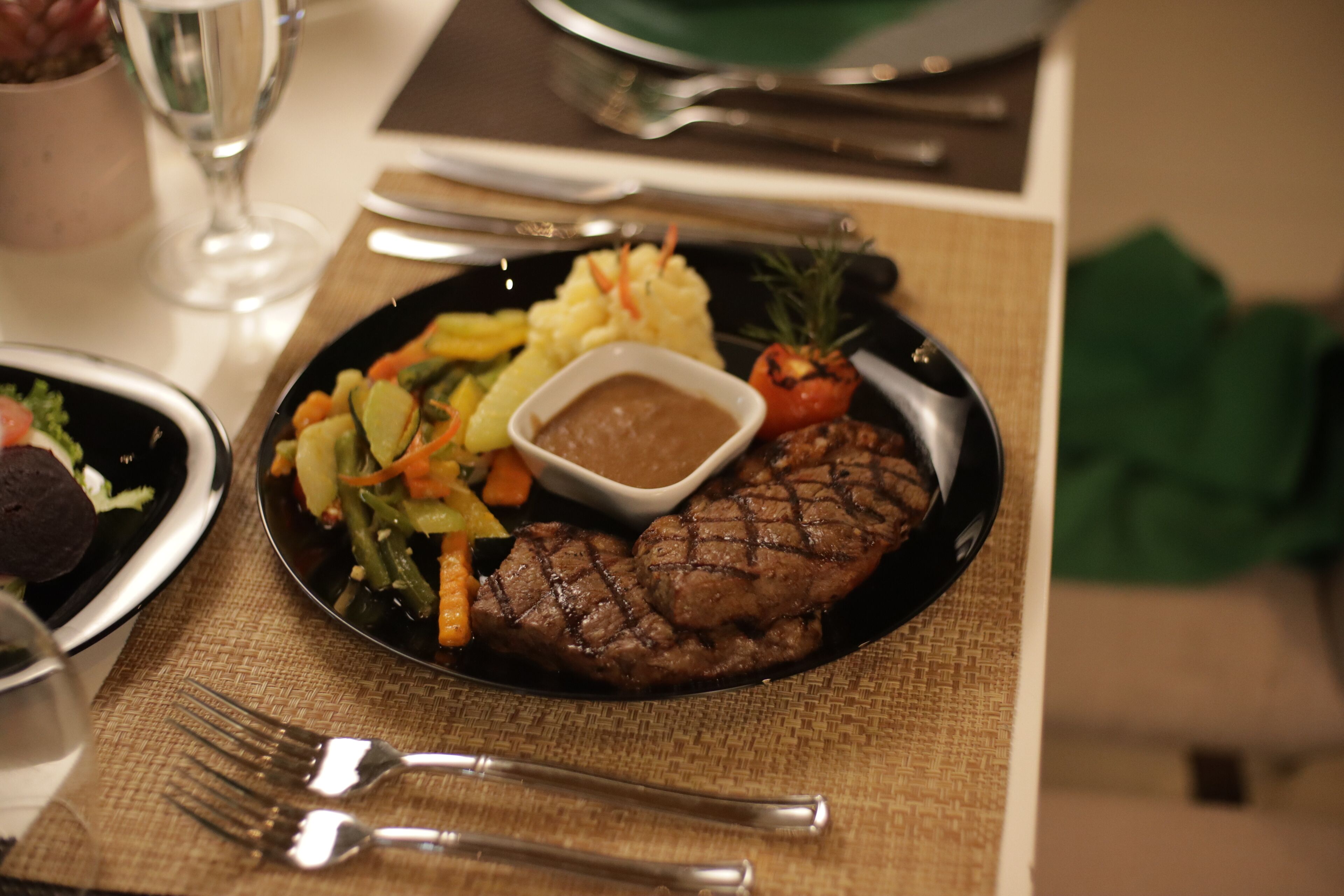 Une assiette de nourriture comprenant un steak, des légumes et une portion de purée de pommes de terre.