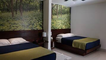Habitación de hotel con dos camas, un ventilador de techo y un gran mural de un bosque en la pared.