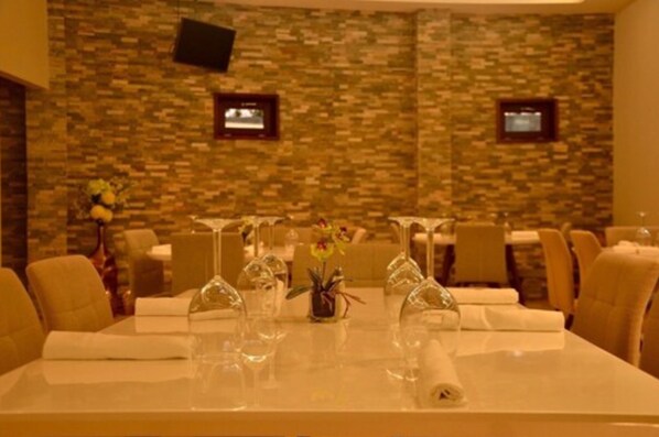A conference room with a stone wall, two screens, and a table set with glassware and flowers. - Hotel Agualcas (Managua)