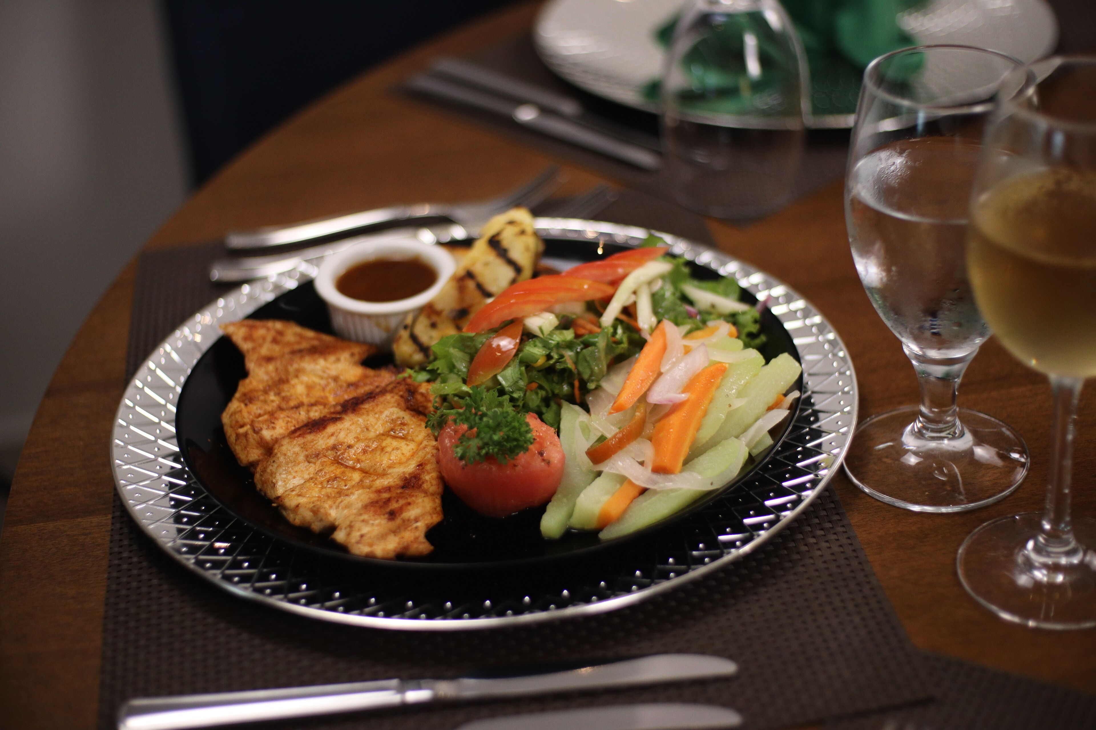 A plate with grilled chicken, a salad, and a small bowl of sauce on a table.