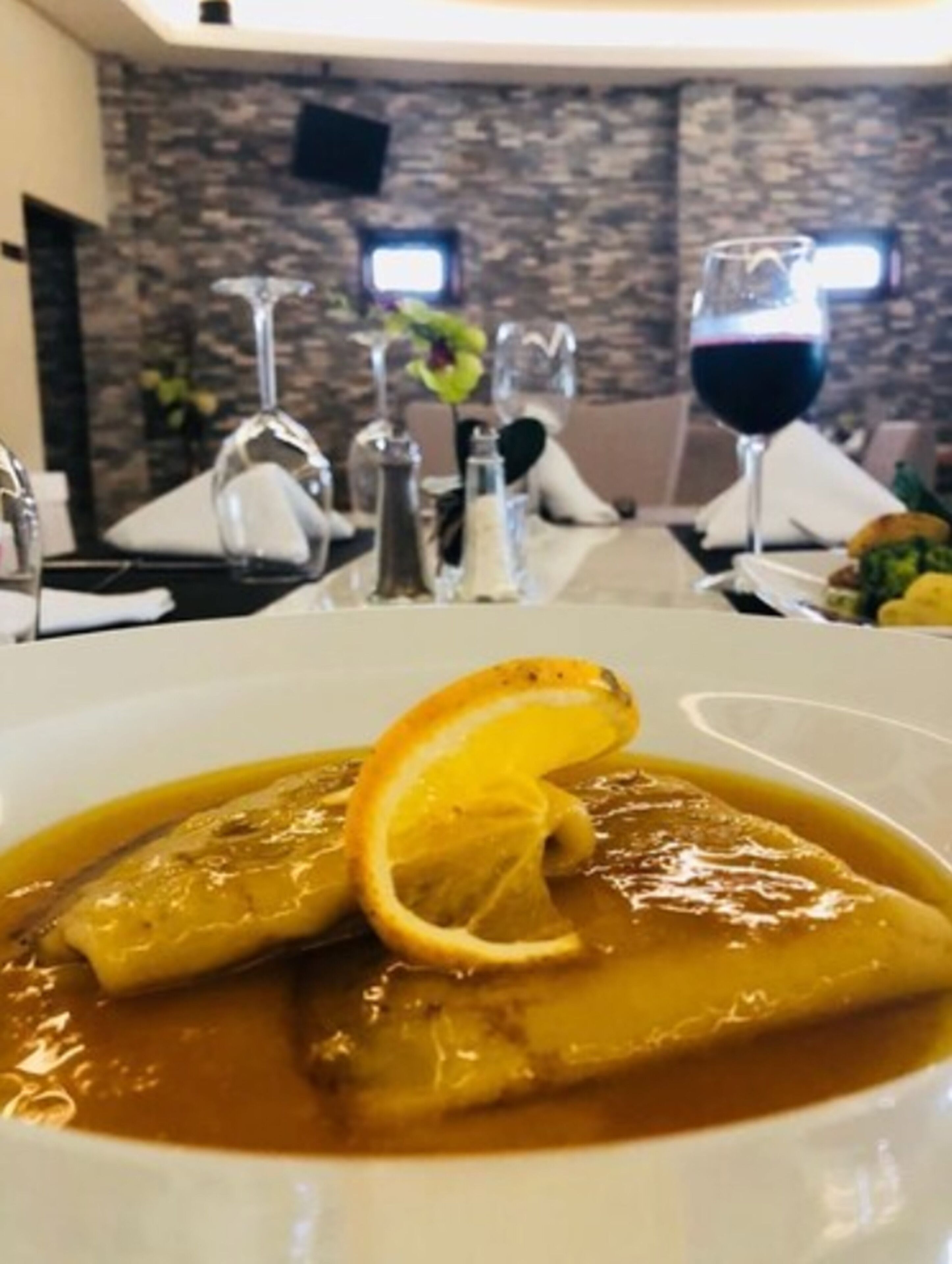 A dining table with a meal, wine glasses, and a stone wall in the background.