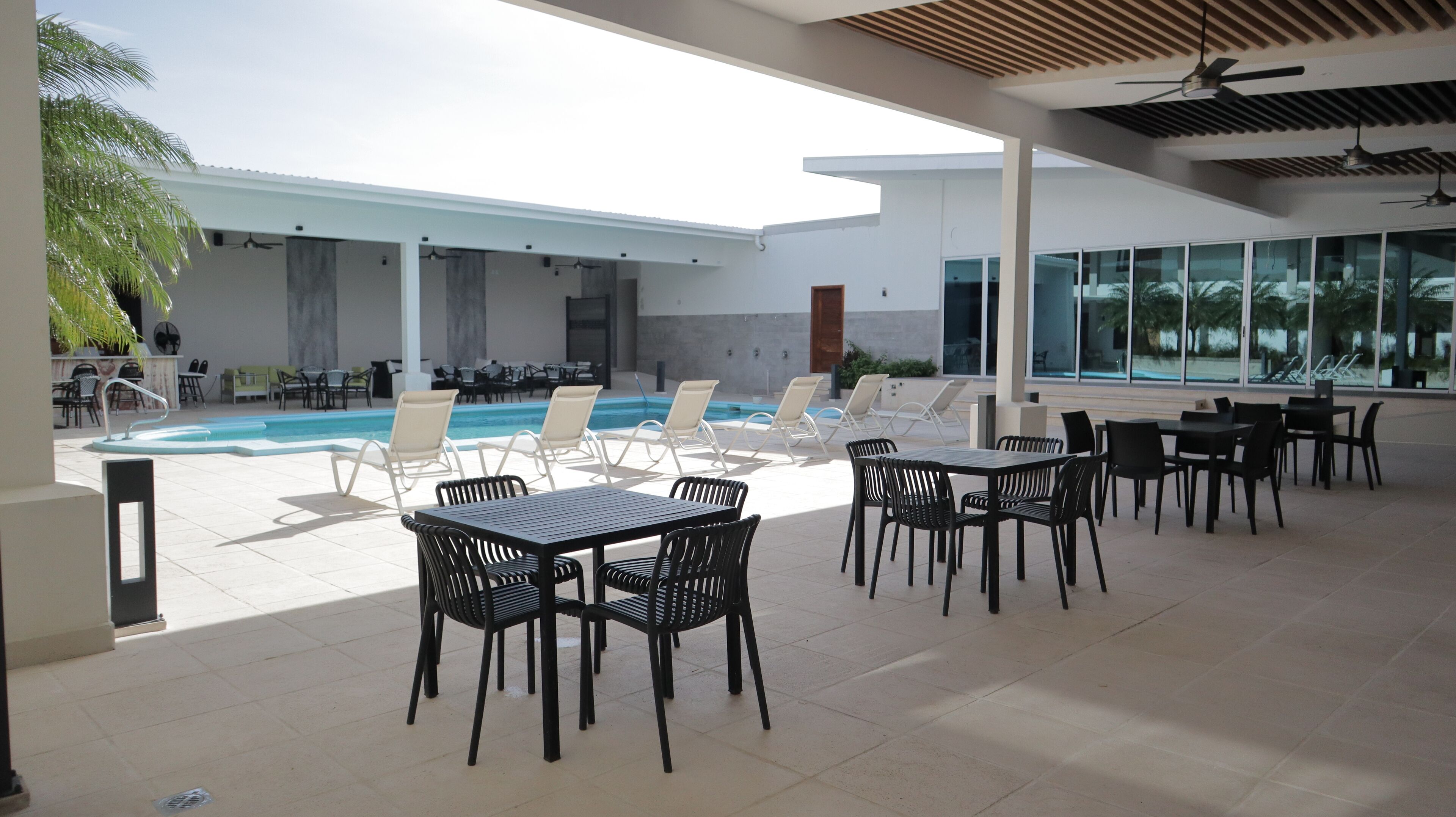Un'area piscina con lettini e tavoli, una piscina e un edificio con ampie finestre.