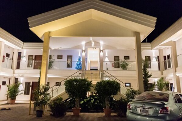 A multi-story hotel with a central staircase, potted plants, and a car parked in front. - Hotel Agualcas (Managua)
