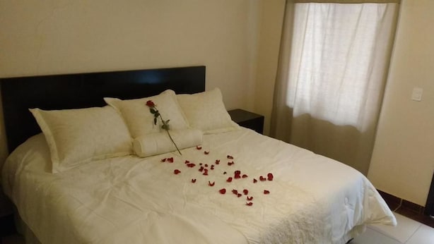 Un lit bien fait, avec du linge de lit blanc et une seule rose posée sur l’oreiller.