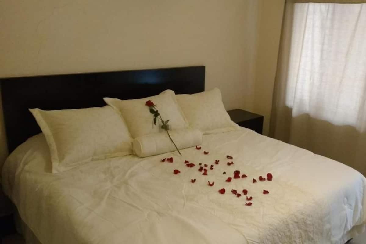 A neatly made bed with white bedding and a single rose on the pillow.