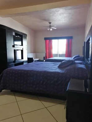 A bedroom with a large bed, a ceiling fan, a TV, and a wardrobe.