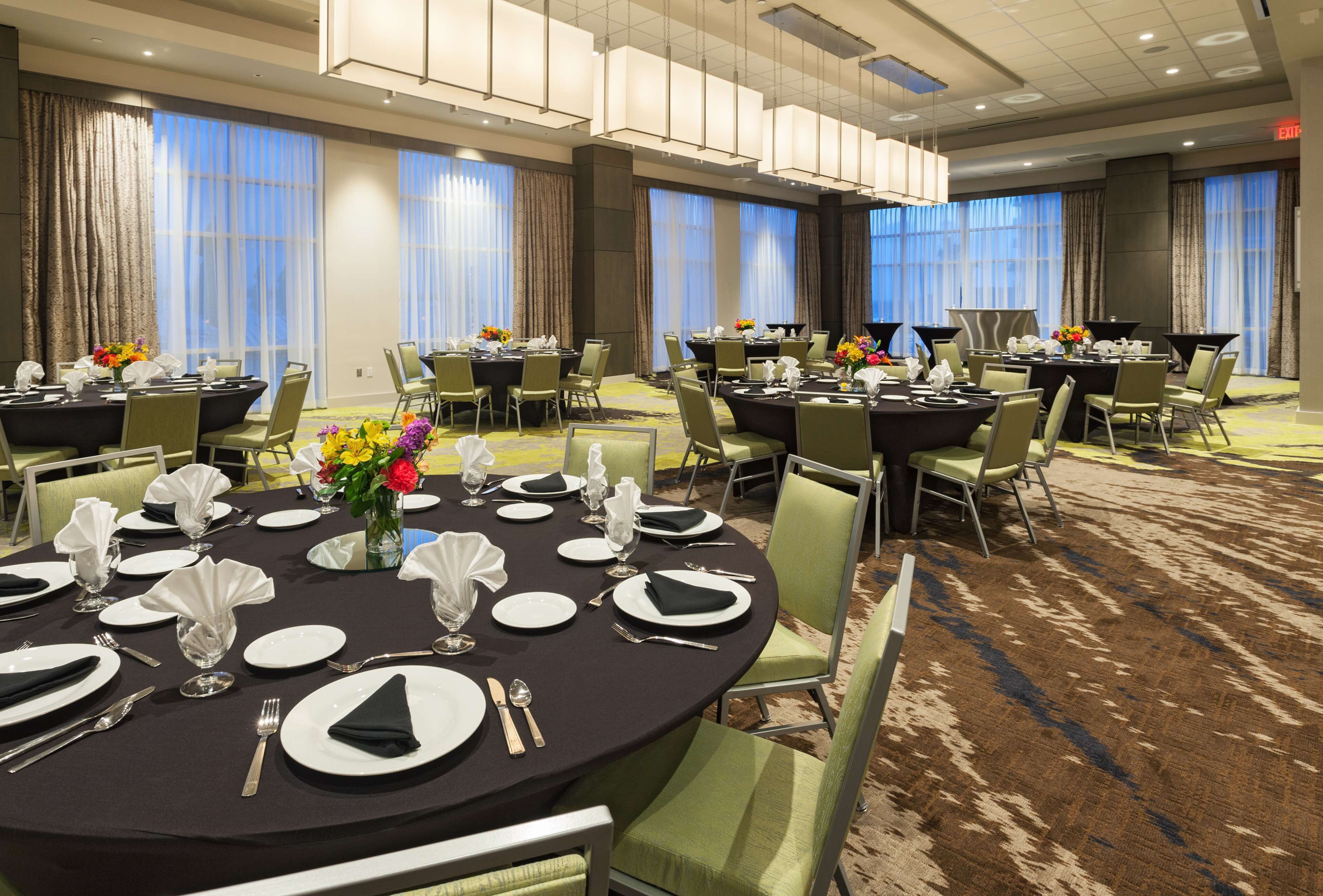 A hotel dining area with multiple round tables set for dining, each with white plates, cutlery, and napkins.