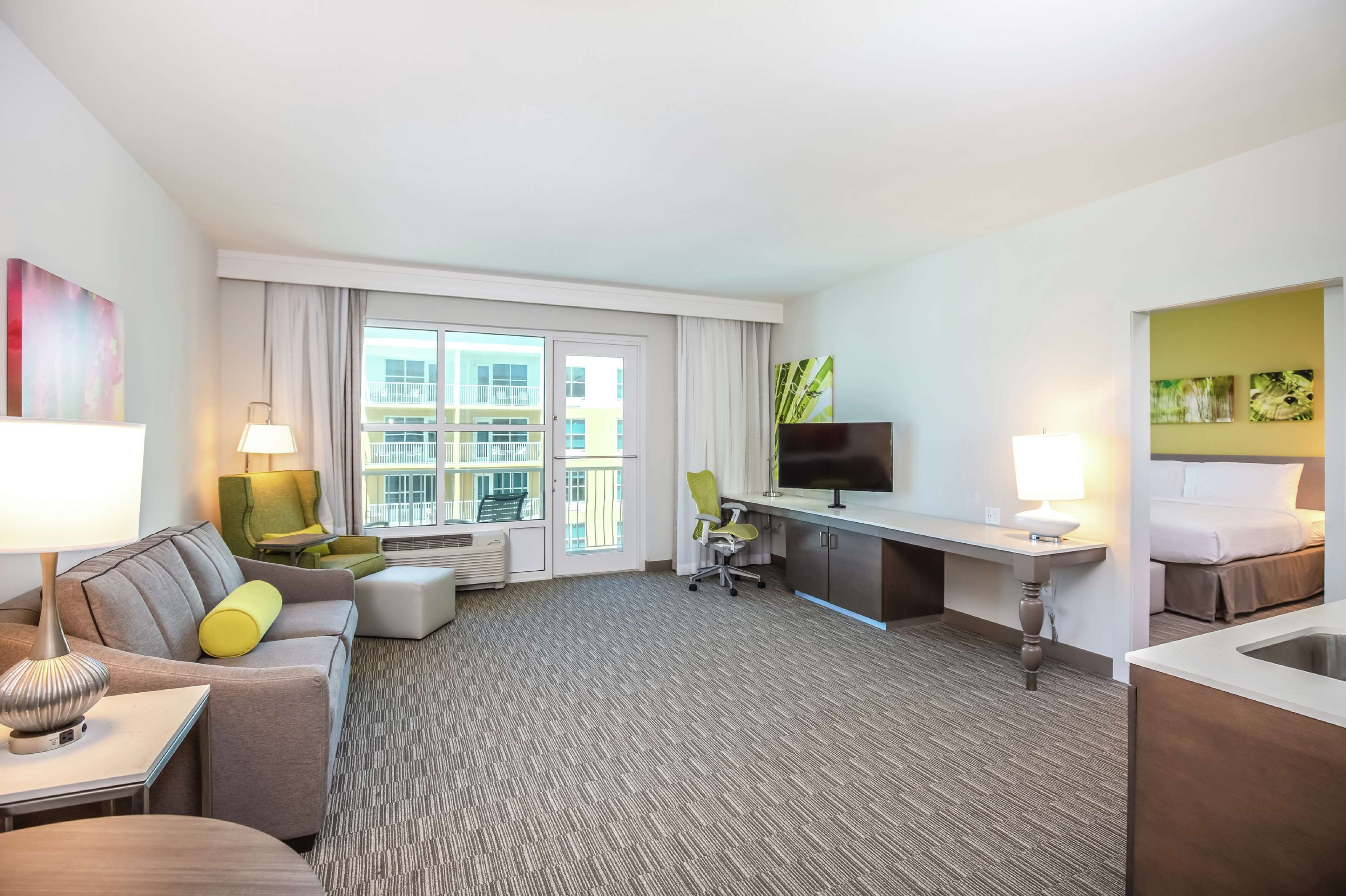 Quarto de hotel com sofá, poltrona, escrivaninha, televisão e cama.