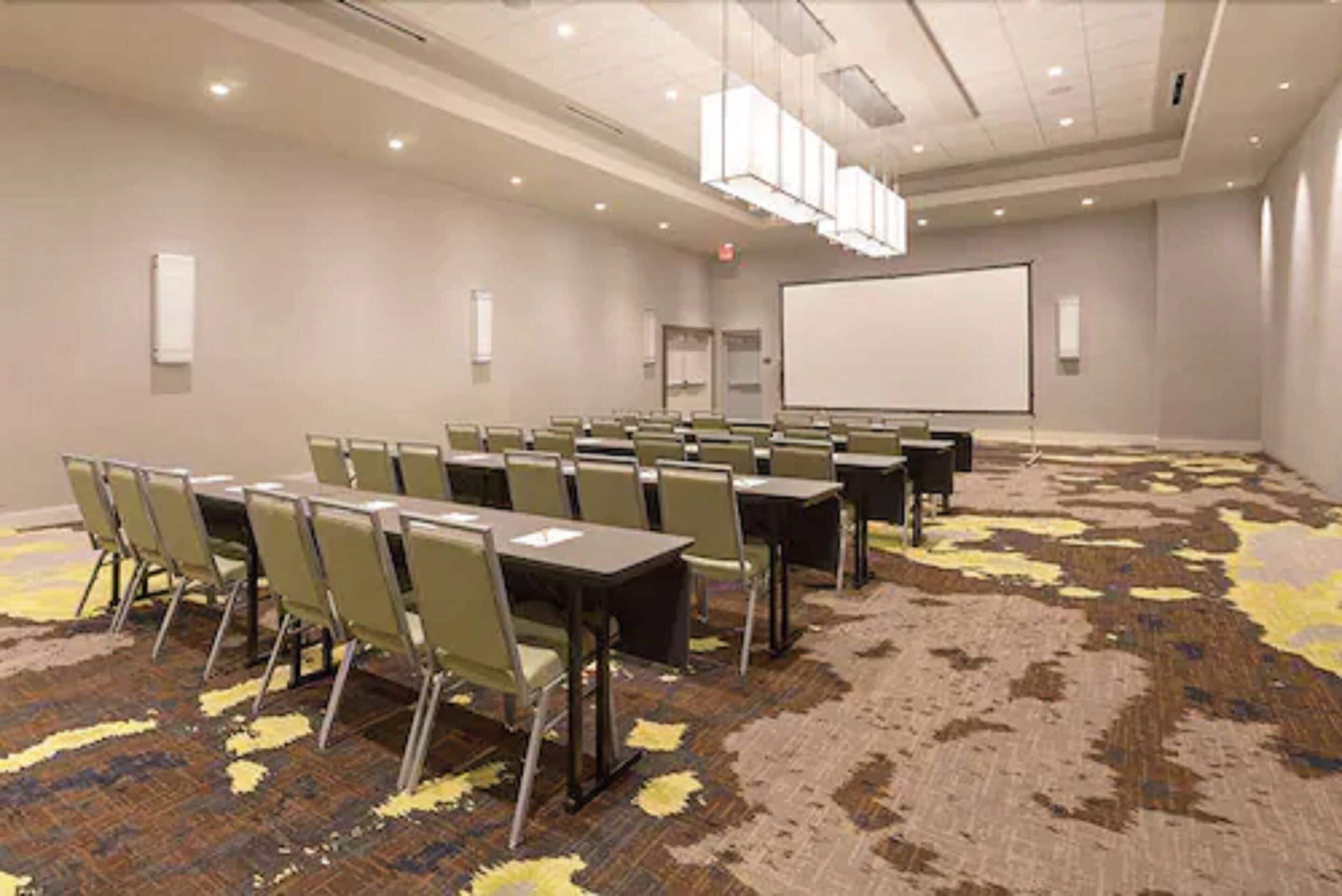Una sala de conferencias con suelo alfombrado, una pizarra y una pantalla para proyector.