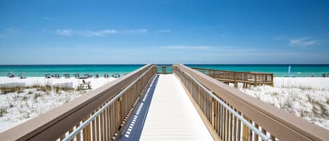 A wooden boardwalk leading to a beach with white sand and turquoise water.