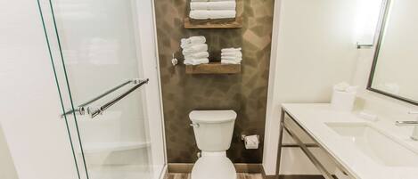 A modern bathroom with a glass shower enclosure, a white toilet, and a sink with a mirror.