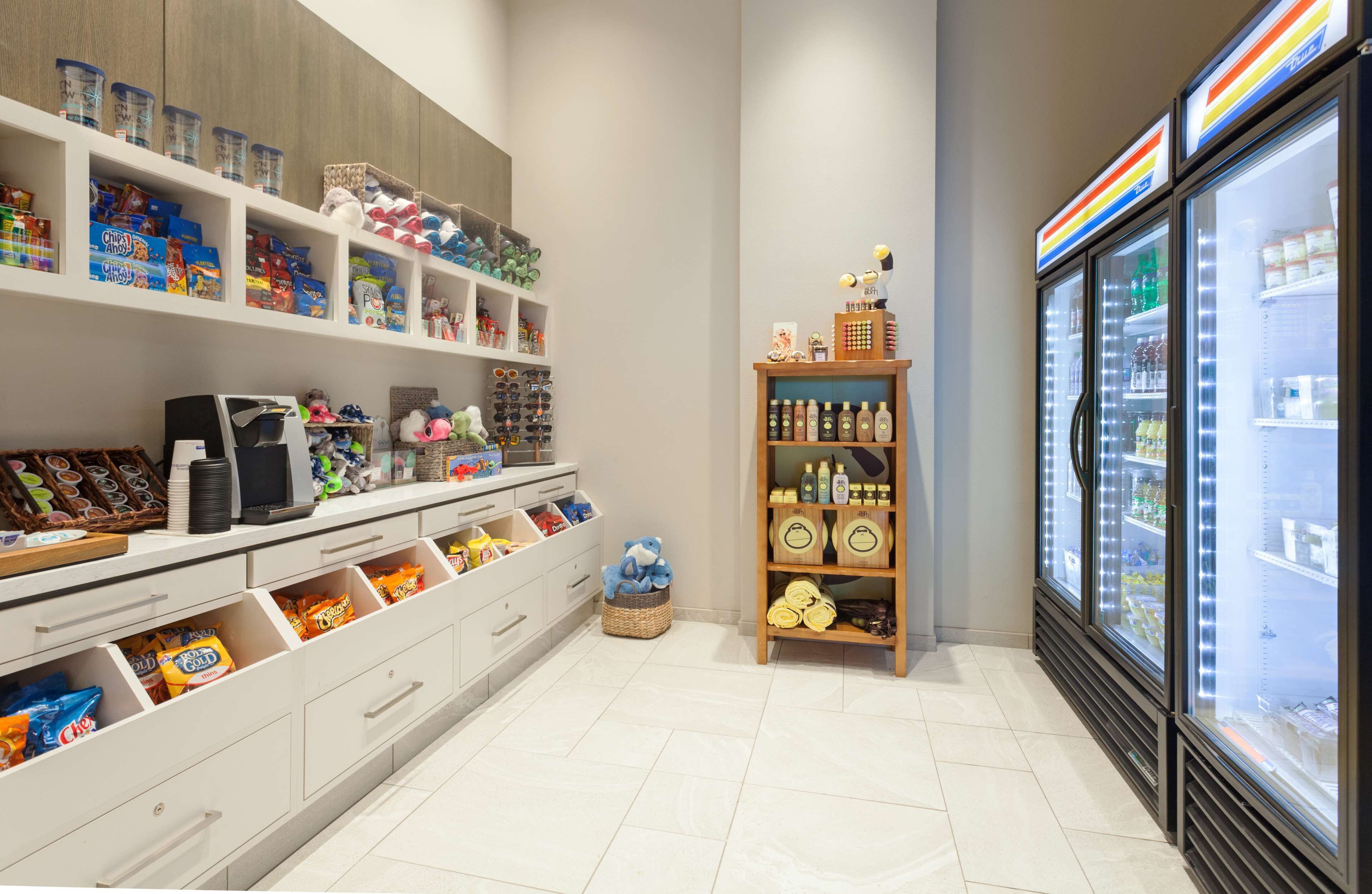A store with shelves stocked with snacks, a refrigerated display, and a wooden shelf with bottles.