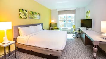 A hotel room with a bed, a desk, a chair, a TV, and artwork on the walls.