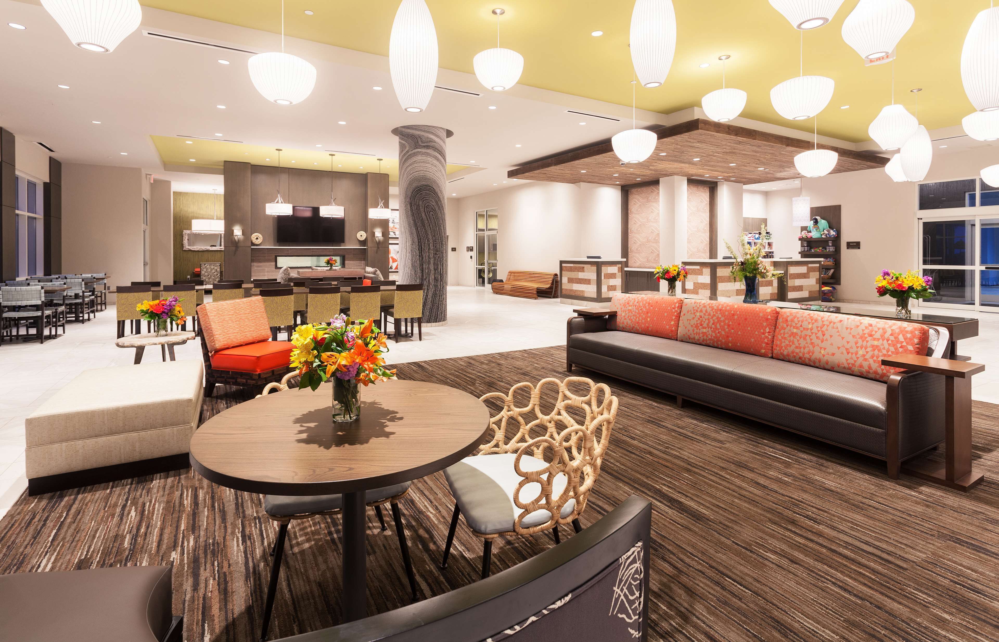 A spacious lobby with a reception desk, seating areas, and a modern kitchen in the background.