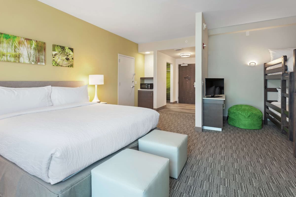 A hotel room with a large bed, a desk, a green bean bag, and a TV.