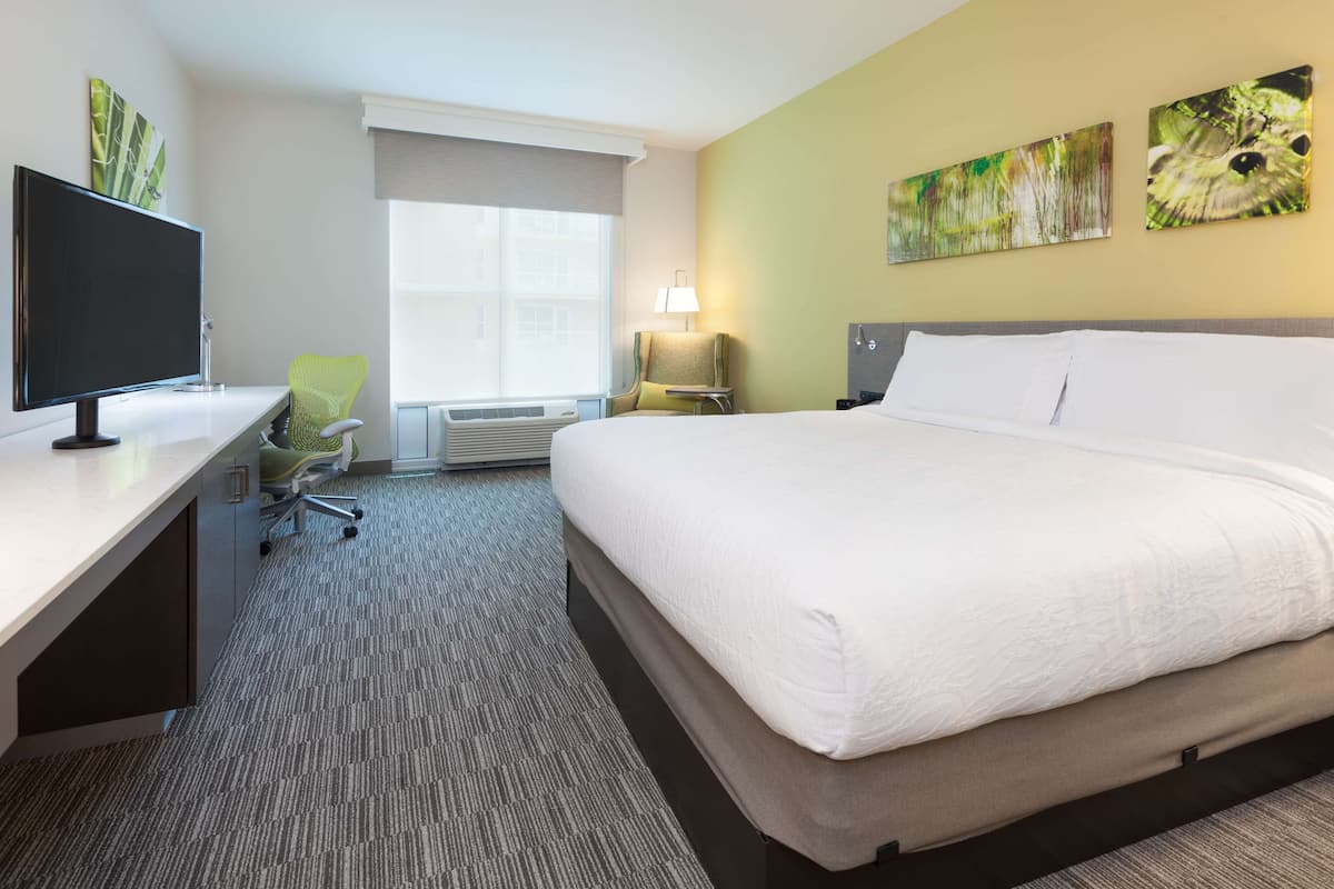 A hotel room with a large bed, a desk with a computer, a chair, and a window with a view.