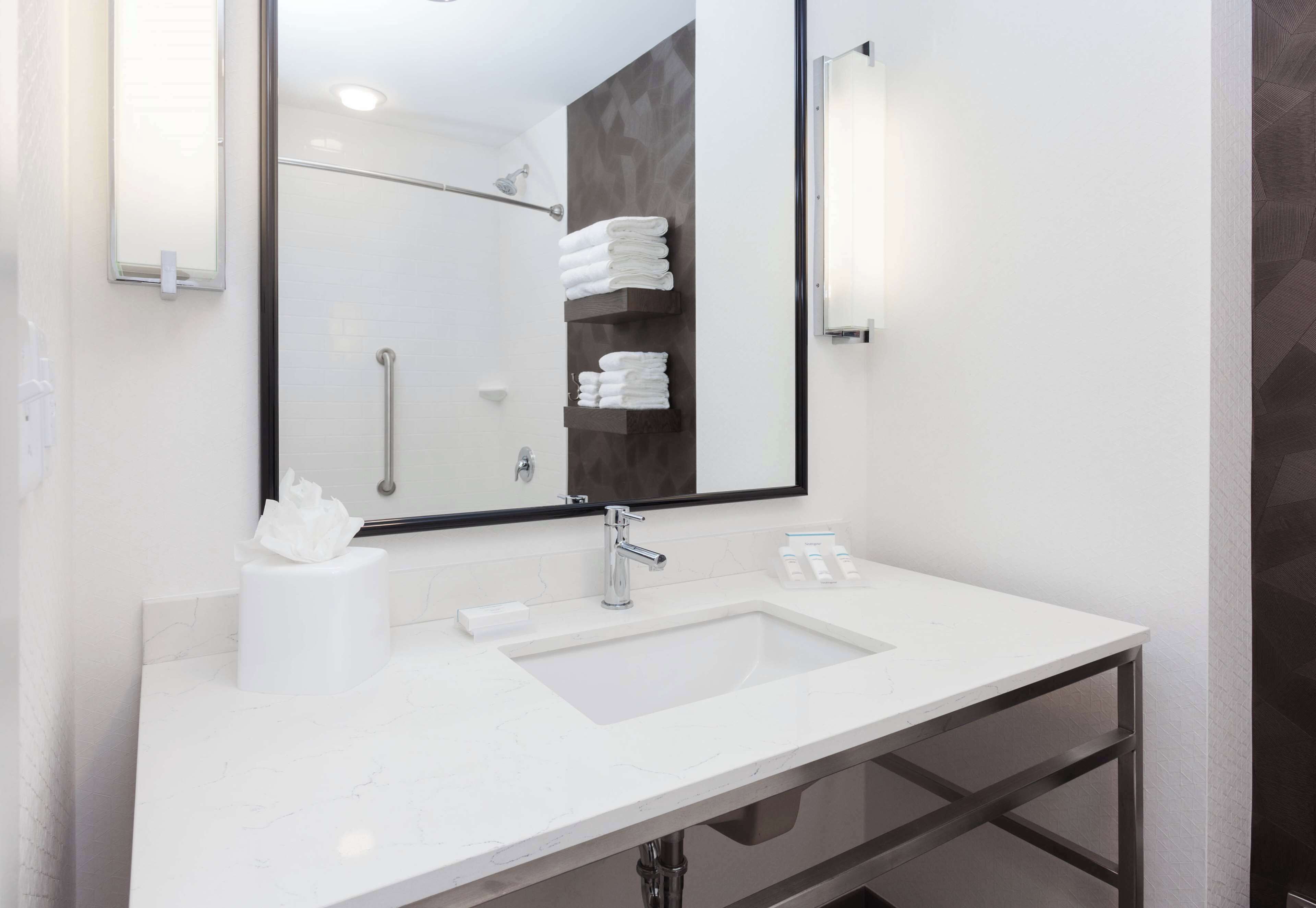 A modern bathroom with a white sink, a large mirror, and a towel rack.