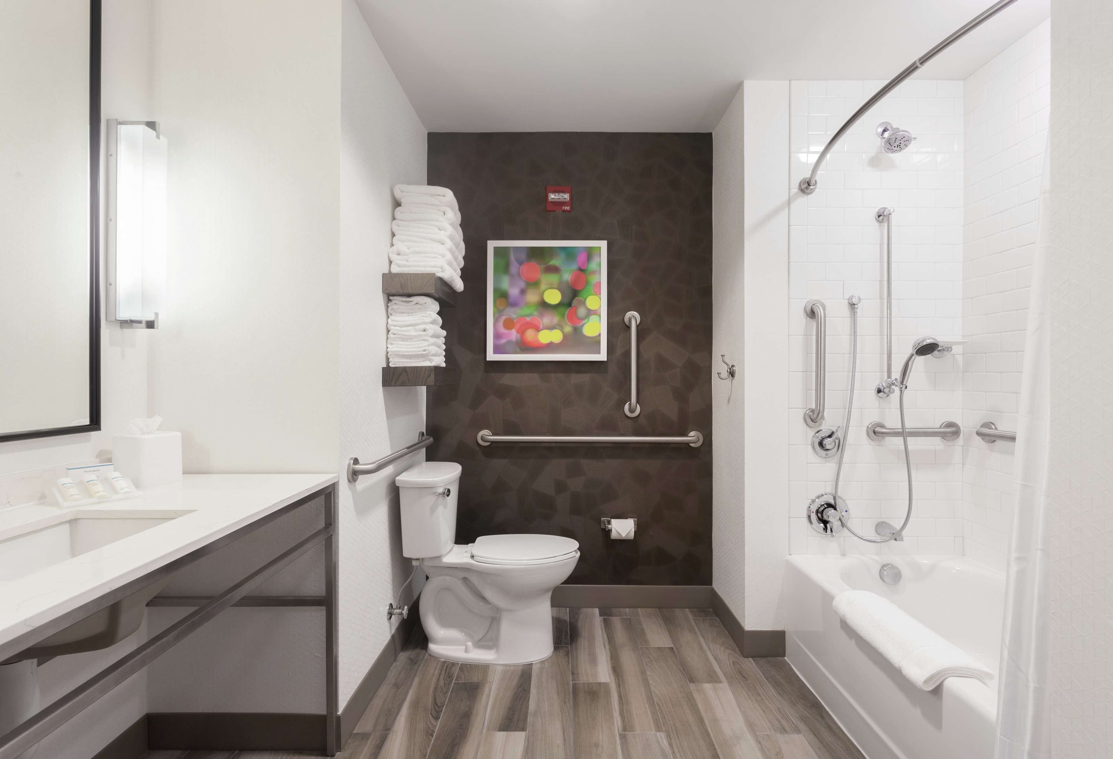 A modern bathroom with a white toilet, a sink, and a shower with grab bars.