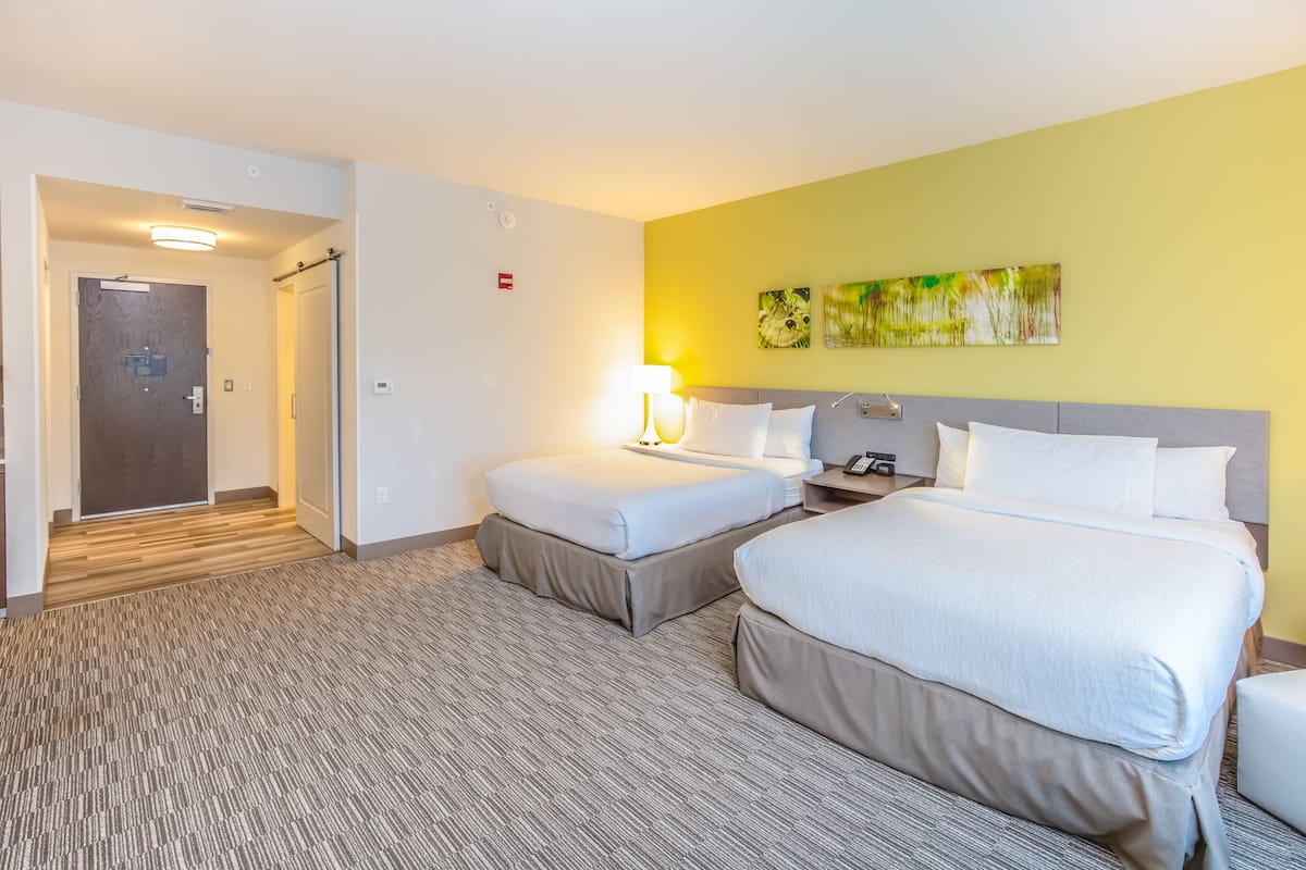 A hotel room with two beds, a nightstand, a lamp, and a painting on the wall.