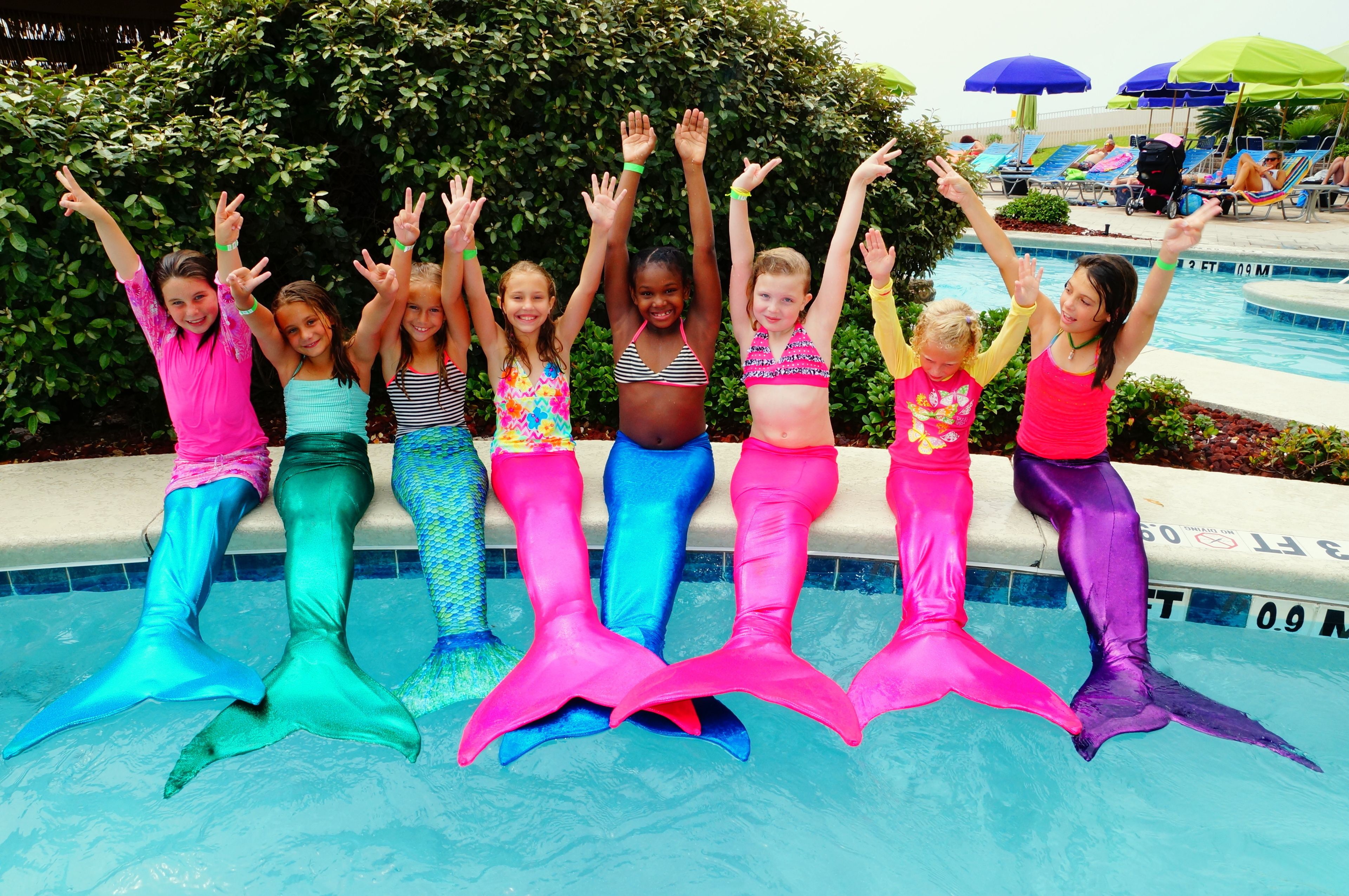 A group of children in mermaid costumes by a poolside.
