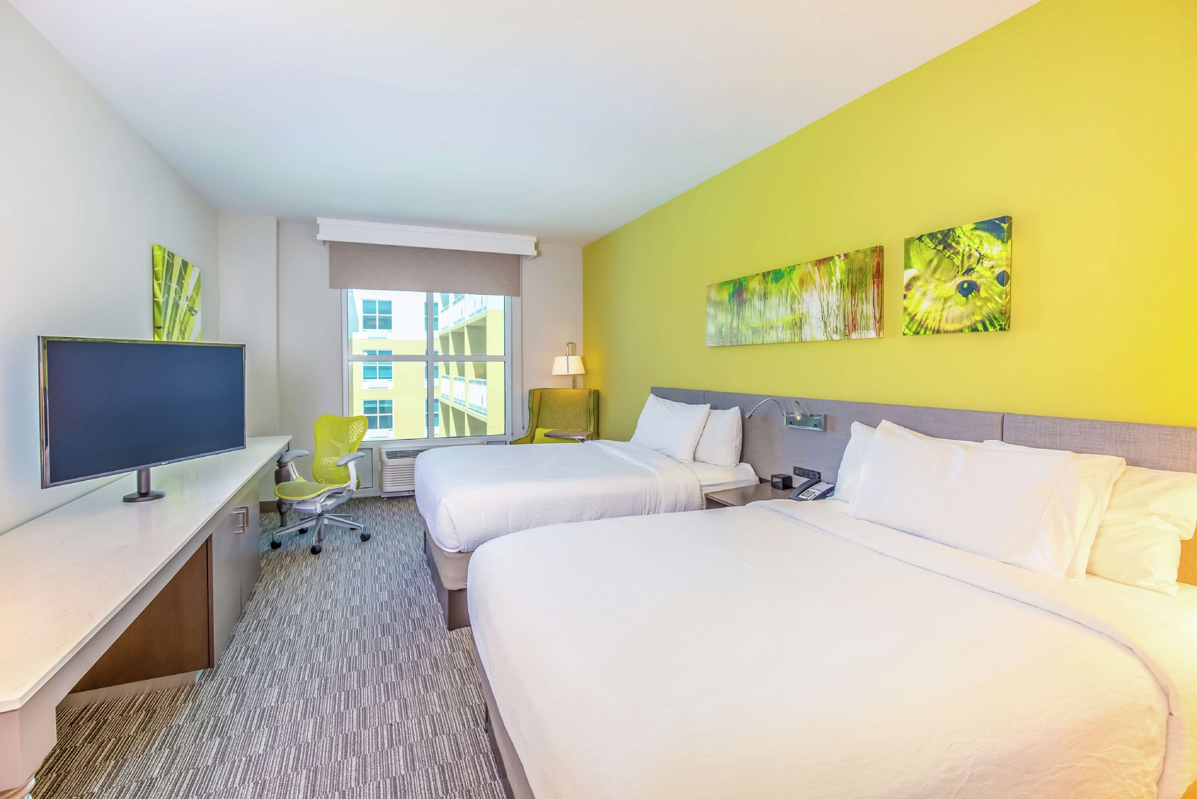 A hotel room with two beds, a desk with a computer, a chair, and artwork on the walls.