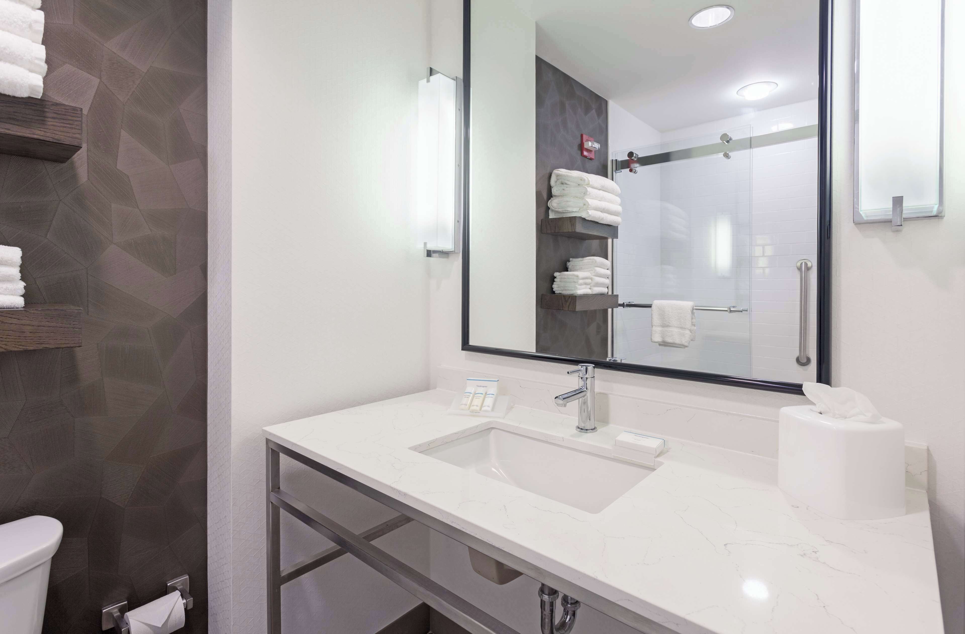 A modern bathroom with a white marble sink, a large mirror, and a glass shower enclosure.