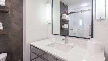 Un baño moderno con lavamanos de mármol blanco, un espejo grande y una cabina de ducha de vidrio.