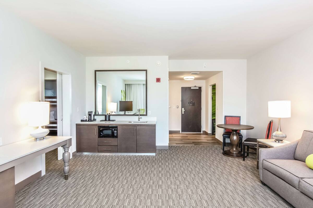 A modern hotel room with a kitchenette, a dining area, and a seating area.